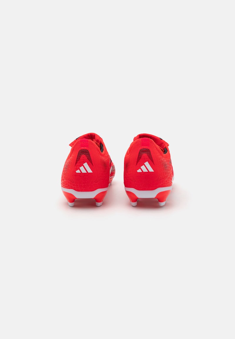 Crampons de foot rouges avec une tige texturée, semelle blanche et accents noirs. Les caractéristiques incluent un design basse et un logo signature sur le talon.