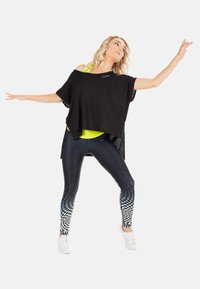 Un top negru supradimensionat pus peste un maieu galben neon, asortat cu colanți negri cu un model gradient în carouri și adidași albi.
