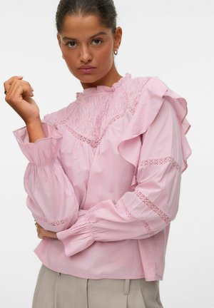 Roze blouse met gerimpelde kraag en mouwen, voorzien van textiel met structuur en geborduurde details langs de naden. Losse pasvorm en wijdvallende mouwen.