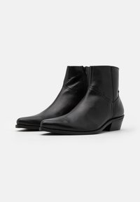 Schwarze Leder-Ankle-Boots mit spitzer Zehe, seitlichem Reißverschluss und einem niedrigen gestapelten Absatz. Glatte Textur mit minimalen Nähdetails.