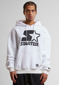 Hvid hættetrøje med et stort sort "STARTER" logo, ribstrikkede manchetter, en kengurulomme og snore til hætten. Blødt, bomuldsblandet materiale.