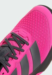 Φωτεινό ροζ αθλητικό παπούτσι με υφασμάτινο επάνω μέρος με υφή, μαύρες λε πτομέρειες και γκρίζες κορδόνες. Έχει τρεις μαύρες ρίγες στο πλάι.