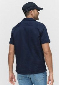 Marineblauw shirt met korte mouwen en een gestreept patroon, met knoopsluiting en een rechte zoom. Gekozen in combinatie met lichtblauwe jeans en een bijpassende pet.