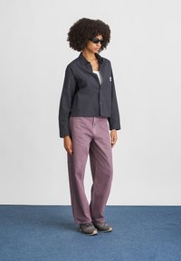 Afskåret navy ternet skjorte, creme top, lilla vide bukser og grå sko. Model iført sorte solbriller står på blå tæppe.