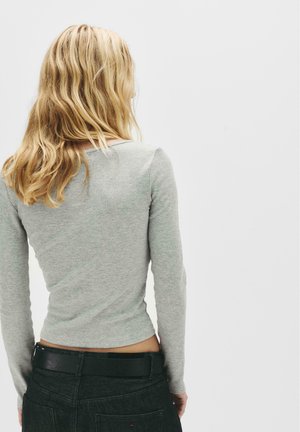 Gray long-sleeve top with a ribbed texture, featuring a low back and a rounded neckline, paired with dark denim and a black belt.