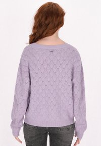 Lila kötött pulóver gyémánt mintával, laza szabású, bordázott mandzsettákkal és szegéllyel. Széles nyakkivágással és texturált anyaggal rendelkezik.