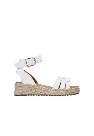 Sandalias espadrilles blancas con suela de yute trenzada, tira para el tobillo con hebilla y un diseño cruzado con detalle de nudo decorativo.