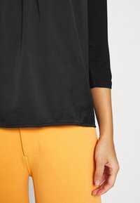 Svart topp i slät tyg med trekvartslånga ärmar, kombinerad med stretchiga, orange byxor med en enkel design.