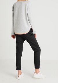 Top gris de manga larga con dobladillo redondeado y una franja multicolor en la parte inferior, combinado con pantalones oscuros entallados y zapatillas blancas.