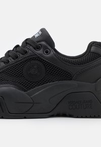 Svarta sneakers som kombinerar mesh- och lädermaterial, rund logopatch, texturerad sula och svarta snören. Märkbart varumärke på hälen.