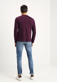 Pitkähihainen violetti paita, puuvillamateriaalia, pyöreä kaulus, yhdistetty vaaleansinisiin farkkuihin, normaali istuvuus, nilkkapituiset, valkoiset ja mustat lenkkarit.