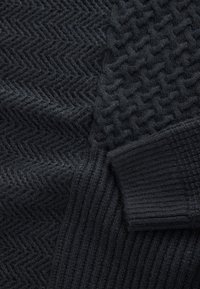 Čierny pletený sveter s rybej kosťou na jednej strane a textúrovaným rebrovaným vzorom na druhej, s jemnou a všestrannou textúrou.