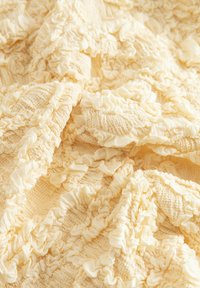 Tissu en crème douce avec des volants texturés et froncés formant un motif de formes circulaires surélevées et de lignes ondulées.
