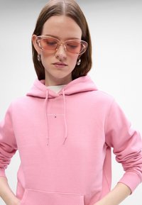 Sudadera de algodón rosa con un bolsillo frontal y capucha con cordón, que presenta un pequeño texto en blanco "TOMMY JEAN" en el pecho.
