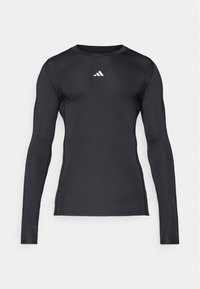 Sort langærmet sportstrøje lavet af glat, strækbart materiale. Har en rund halsudskæring og et diskret hvidt logo på brystet.