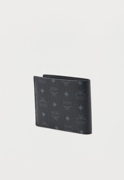 Μαύρο δερμάτινο πορτοφόλι με υφή που διαθέτει διαμαντένια σχέδια. Το λογότυπο MCM είναι διακριτικά ανάγλυφο σε όλη την επιφάνεια. Σχεδίαση διπλής όψης, συμπαγής μορφή.