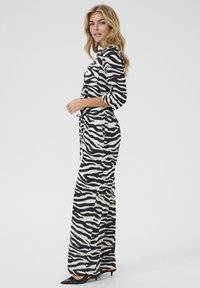 Svart och vit zebra-mönstrad jumpsuit med trekvartsärmar, insvängd midja och vida ben. Stylingen kompletteras med svarta spetsiga klackskor.