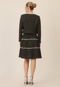 Vestido de tweed negro con un cuerpo ajustado, falda de tres capas y acentos en blanco. Sandalias de tacón alto plateadas completan el look.