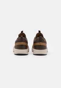 Chaussures brunes avec une tige texturée, présentant des accents beiges contrastants, une semelle rembourrée et des languettes au talon pour un enfilage facile.