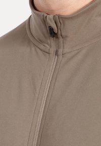 Braune ZIP-Jacke mit hohem Kragen, ausgestattet mit glatter Textur und figurbetontem Schnitt, hervorgehoben durch kontrastierende Nähte entlang des Reißverschlusses.