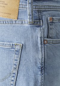 Jeans in denim blu chiaro con un design standard a cinque tasche, cuciture visibili e un'etichetta in pelle sul fascione posteriore.