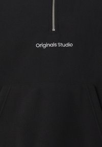 Mustaveläkkipaidan puoliväli vetoketjulla, jossa on etutasku; "Originals Studio" brodeerattu valkoisella. Pehmeä rakenne ja minimalistinen muotoilu.