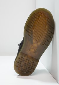 Black shoe sole with a textured rubber pattern, featuring a semi-transparent brown outsole and a rectangular logo imprint.