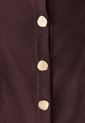 Vīna krāsas audums ar pieciem dabīgiem pogām, kas veidotas kā gliemežvāki. Pogām ir teksturēts dizains, kas kontrastē ar gludo materiālu.