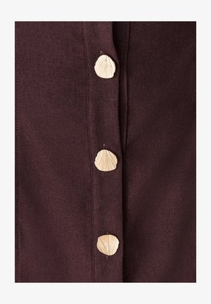 Vīna krāsas audums ar pieciem dabīgiem pogām, kas veidotas kā gliemežvāki. Pogām ir teksturēts dizains, kas kontrastē ar gludo materiālu.