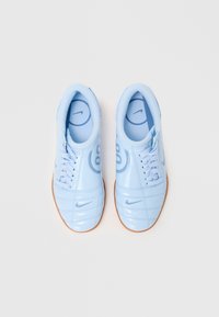 Sapatilhas atléticas de azul claro com um acabamento brilhante, apresentando atacadores planos, laterais texturizadas e uma sola de borracha. Logotipo da Nike visível na língua.