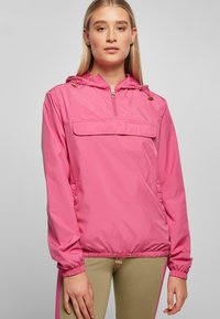Roze lichtgewicht jas met een capuchon, een rits aan de voorkant en een kangaroo zak. Beschikt over trekkoorden aan de onderkant en op de manchetten voor een verstelbare pasvorm.