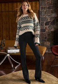 Pulover tricotat crem cu modele geometrice verzi și mâneci oversized, asortat cu blugi negri mulați și cizme negre cu toc.