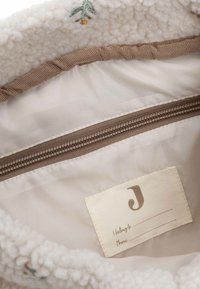 Tan-kleurig stoffen interieur met een rits, met crèmekleurig textuurmateriaal en een geborduurd ontwerp. Inclusief een label voor personalisatie.