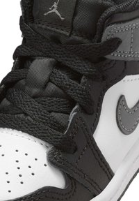 Sneaker in bianco e nero con materiali in pelle e mesh, caratterizzato da una linguetta nera testurizzata, stringhe prominenti e il logo swoosh Nike grigio.