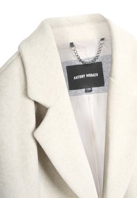 Abrigo de mezcla de lana beige con un diseño a medida, solapas muesca y un interior de satén. Presenta una etiqueta de Antony Morato y un detalle de cadena.