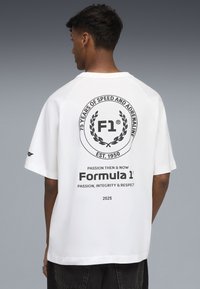 Biała, oversize koszulka z krótkim rękawem, z czarną, okrągłą grafiką z napisem "F1". Wykonana z bawełny, bez dodatkowych ozdób na froncie.