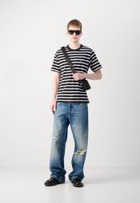 Striped black and white T-shirt, blue distressed baggy jeans, black sunglasses, and a small black crossbody bag. Smooth fabric and relaxed fit.