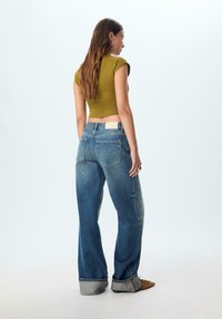 Khaki krátky top s rukávmi po rameno v kombinácii so svetlomodrými širokými nohavicami so skladaným lemom a koženou visačkou na opasku.