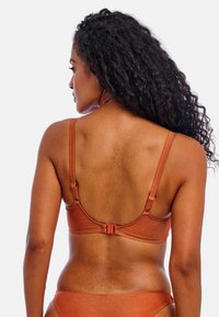 Bra in rust color with a smooth texture, adjustable straps, and a clasp at the back. Subtle sheen visible on the fabric.