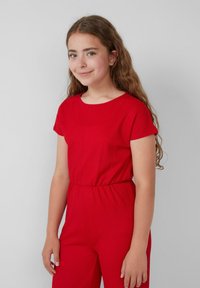 Combinaison en coton rouge avec des manches courtes, un col rond et une taille élastique. Tissu texturé et forme ajustée. Design simple et épuré.