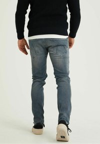 Jeans blu chiari con taglio slim, dettagli strappati, due tasche posteriori e finitura sbiadita, abbinati a sneakers nere.