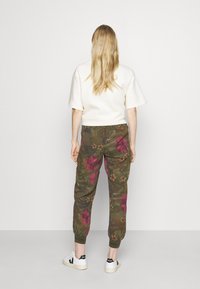 Khaki cargobroek met een bloemenpatroon in roze en groene tinten. Gemaakt van katoen, met taps toelopende boorden en zijzakken. Draag het met een top met korte mouwen.