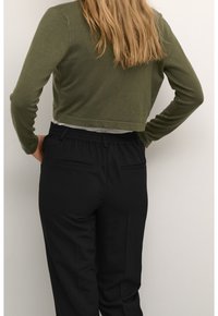 Pull olive vert coupé avec de longues manches et un ourlet arrondi, associé à un pantalon noir avec une taille élastique et des poches latérales.