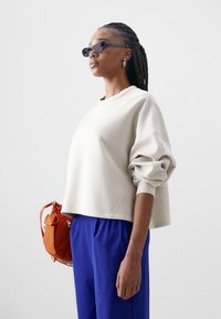 Mala de mão pequena laranja e óculos de sol escuros.