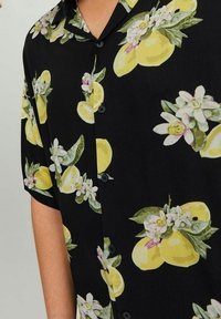Zwart T-shirt met korte mouwen met een citroen- en bloemenprint. Gemaakt van lichtgewicht stof met een knoopsluiting aan de voorkant en een zachte textuur.