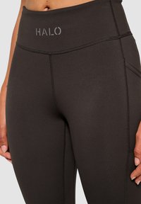 Svarta högmidjade leggings med en slät yta, prydda med en grå "HALO"-logotyp, synliga sömmar och sidofickor.