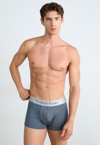 Boxers ajustados Calvin Klein en gris con una cinturilla plateada. Tejido suave, ajuste ceñido, diseño minimalista y sin patrones visibles.