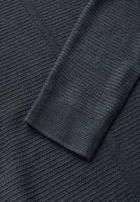 Schwarzer Stoff mit einer strukturierten Rippenmusterung und glatten Akzenten. Das Material wirkt leicht und weich und zeigt feine gewebte Details.