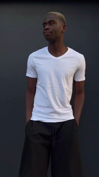 Camiseta blanca de manga corta y cuello en V combinada con pantalones cortos negros de corte holgado. El modelo está de pie con las manos en los bolsillos, frente a un fondo oscuro.