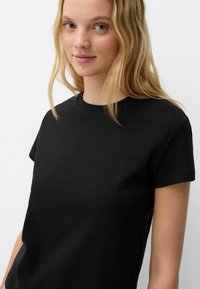 Tricou din bumbac negru, cu mâneci scurte, de formă rotundă la gât și textură netedă. Design simplu, fără modele sau accesorii vizibile.